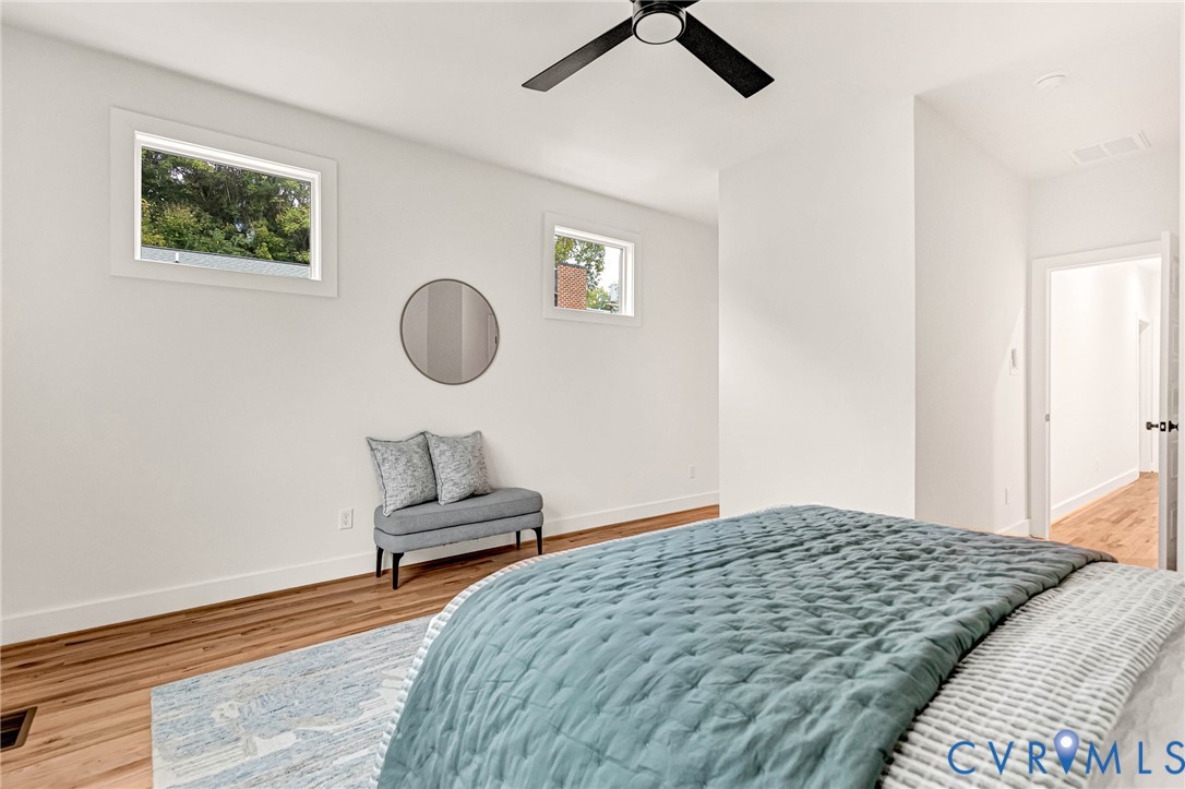 Bright room featuring wood-finish flooring, two high-set rectangular windows, and a black ceiling fan