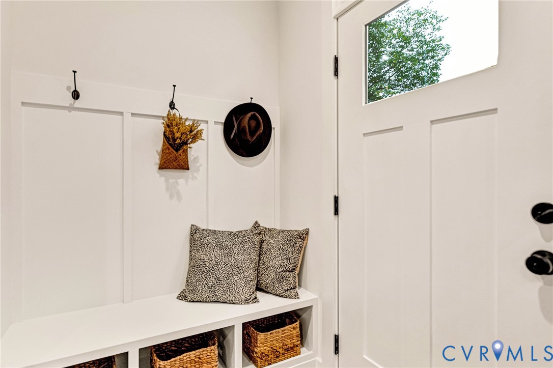 Entryway featuring a white exterior door with a glass inlay, matte black hardware, built-in bench seating with lower storage compartments, and white board-and-batten wall detailing with mounted metal hooks