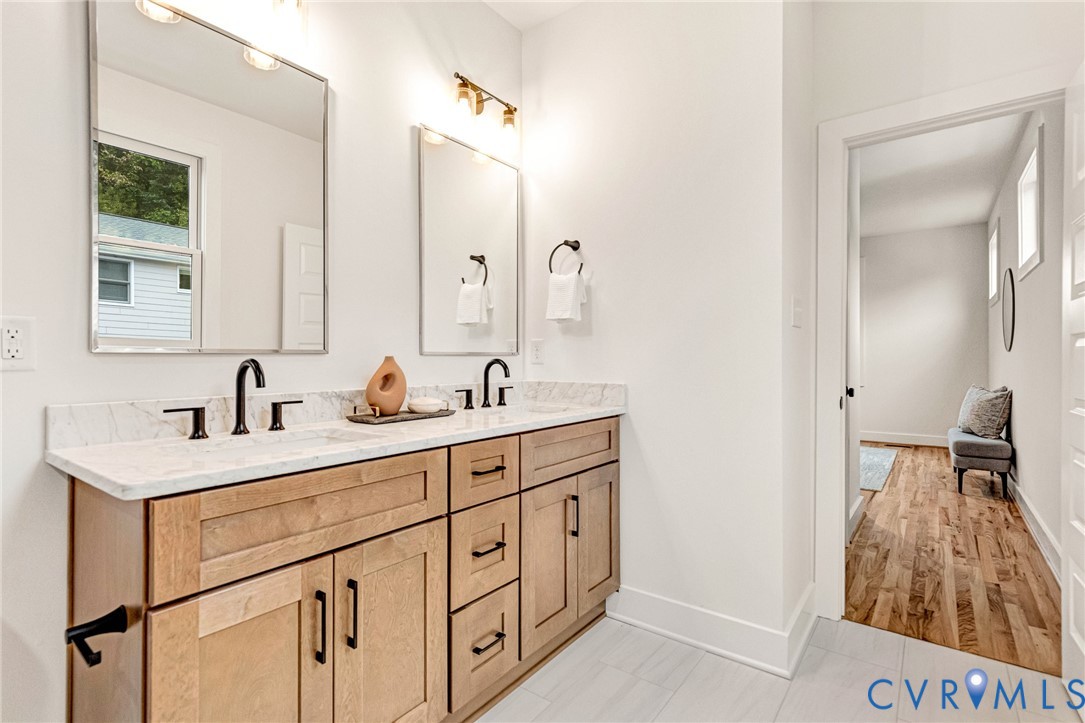 Dual-sink vanity with light wood-finish cabinetry, stone countertop, matte black fixtures, and two rectangular wall-mounted mirrors
