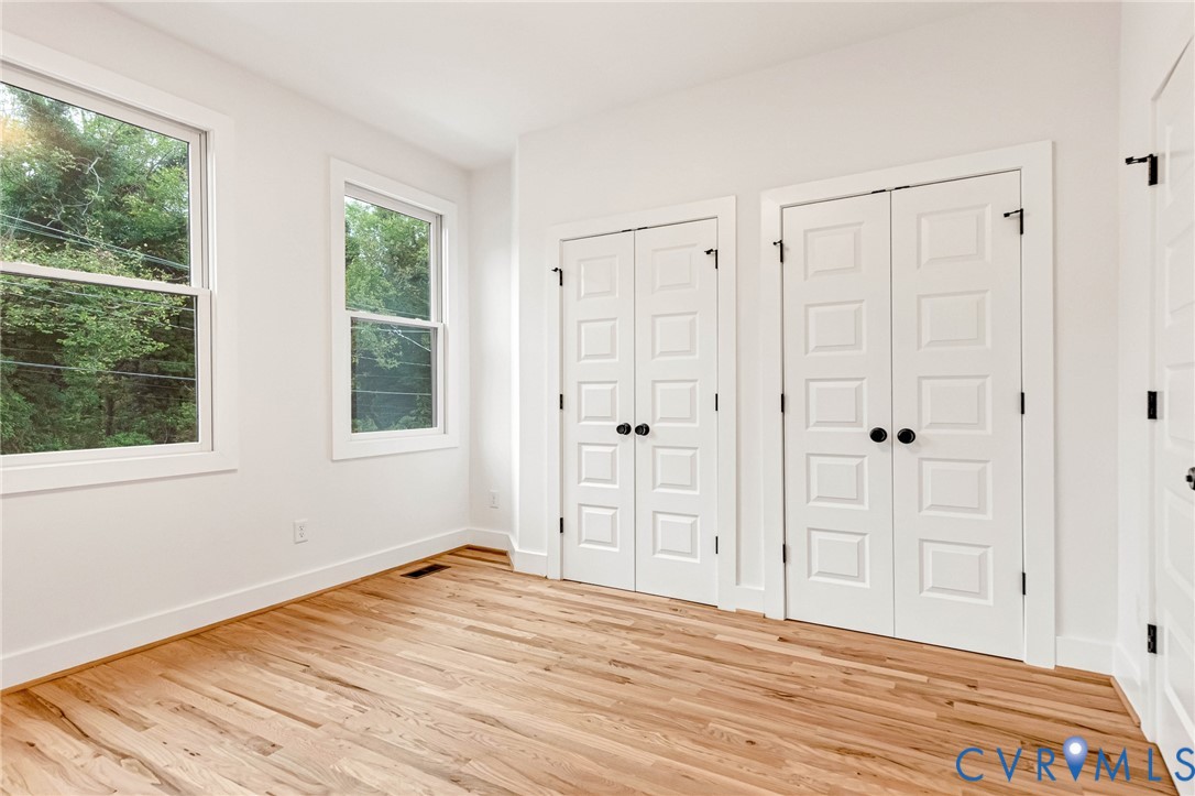 Wood-finish flooring, dual double-door closets with matte black hardware, and two large windows with natural illumination