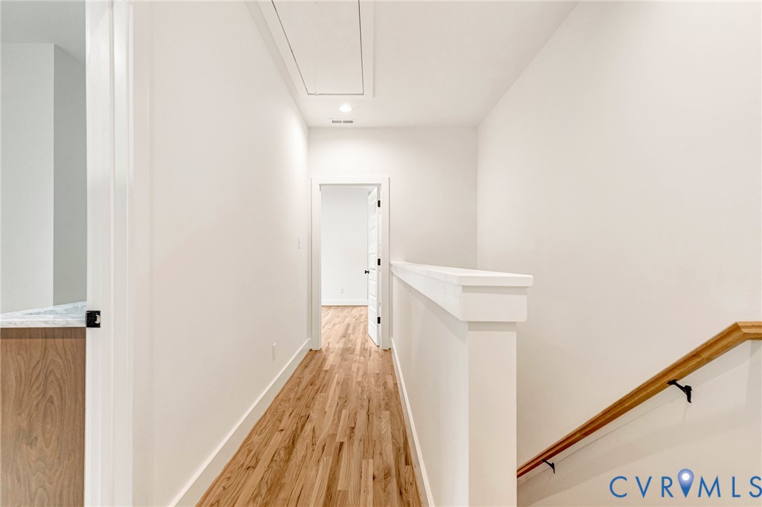 Hallway featuring wood-finish flooring, a solid half-wall partition, and a natural wood-finish handrail with matte black hardware
