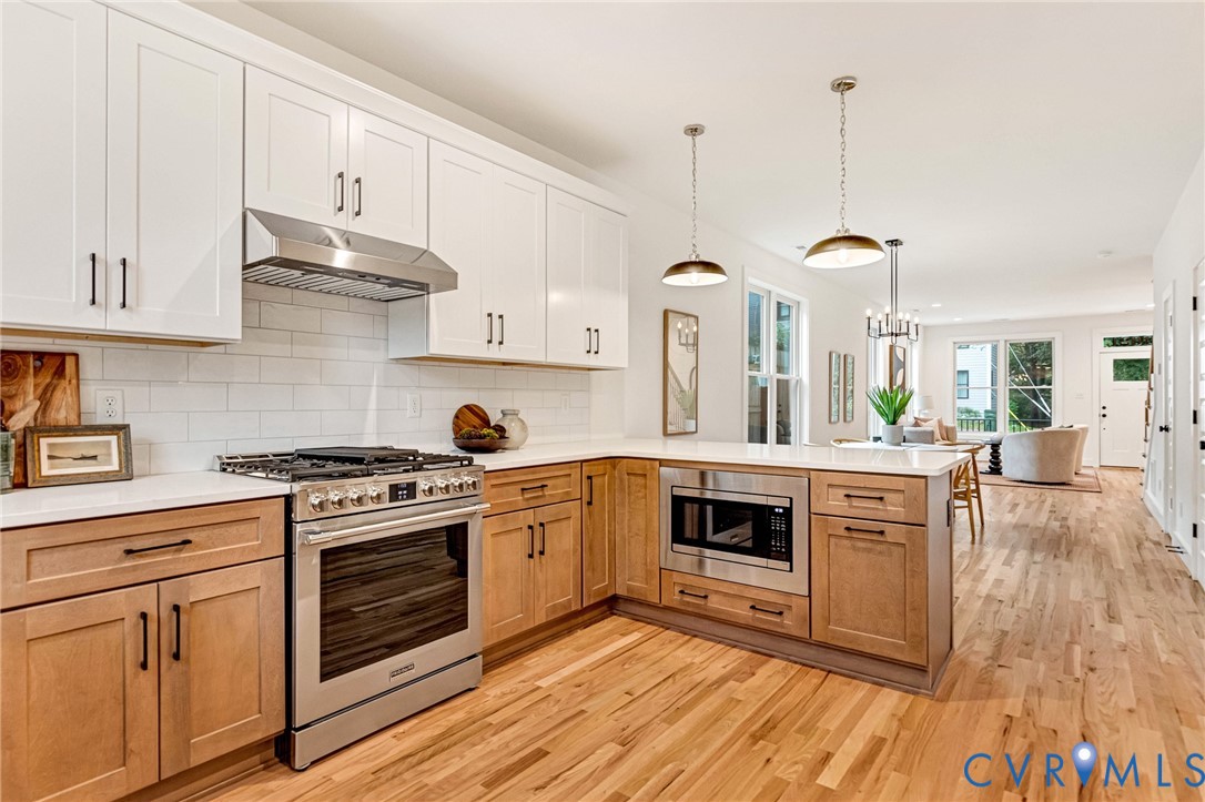 Kitchen featuring two-tone cabinetry with white upper cabinets and light wood-finish base cabinets, subway tile backsplash, stainless steel gas range, built-in microwave, and wood-finish flooring