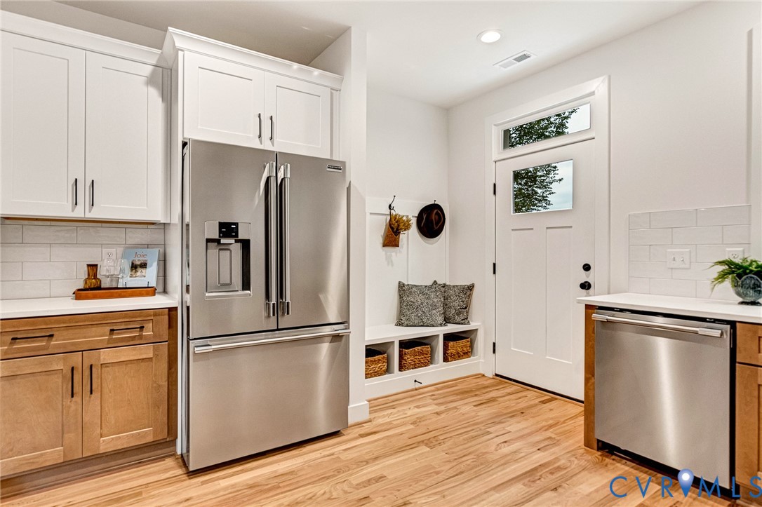 Kitchen featuring wood-finish cabinetry, white upper cabinetry, stainless steel appliances, subway tile backsplash, and built-in bench seating