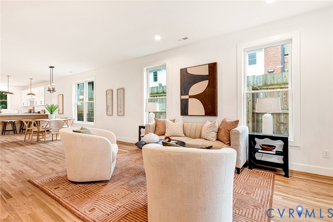 Open-concept living space featuring wood-finish flooring, recessed lighting, multiple oversized windows, and crisp white walls