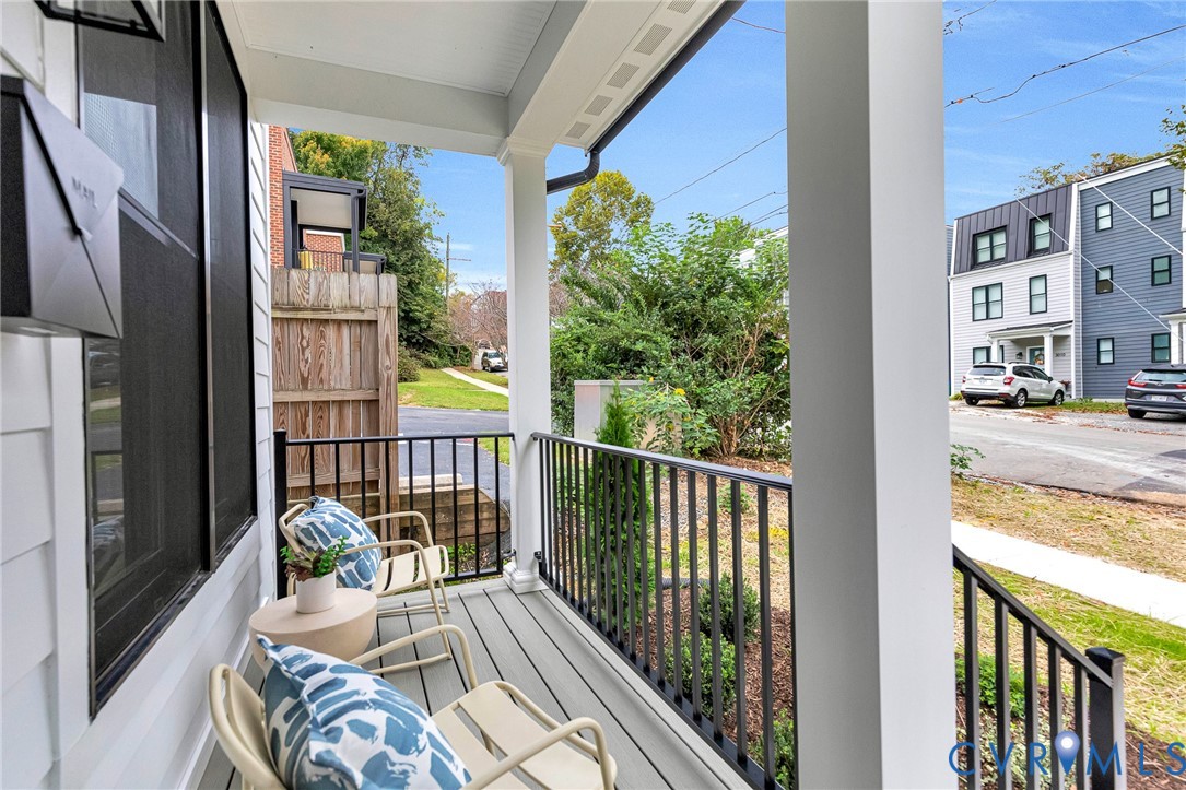Covered front porch featuring gray composite decking, black metal railings, and square support columns