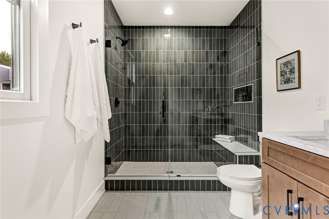 Walk-in shower featuring vertical charcoal tile, frameless glass enclosure, built-in bench seating, recessed wall niche, and matte black plumbing fixtures