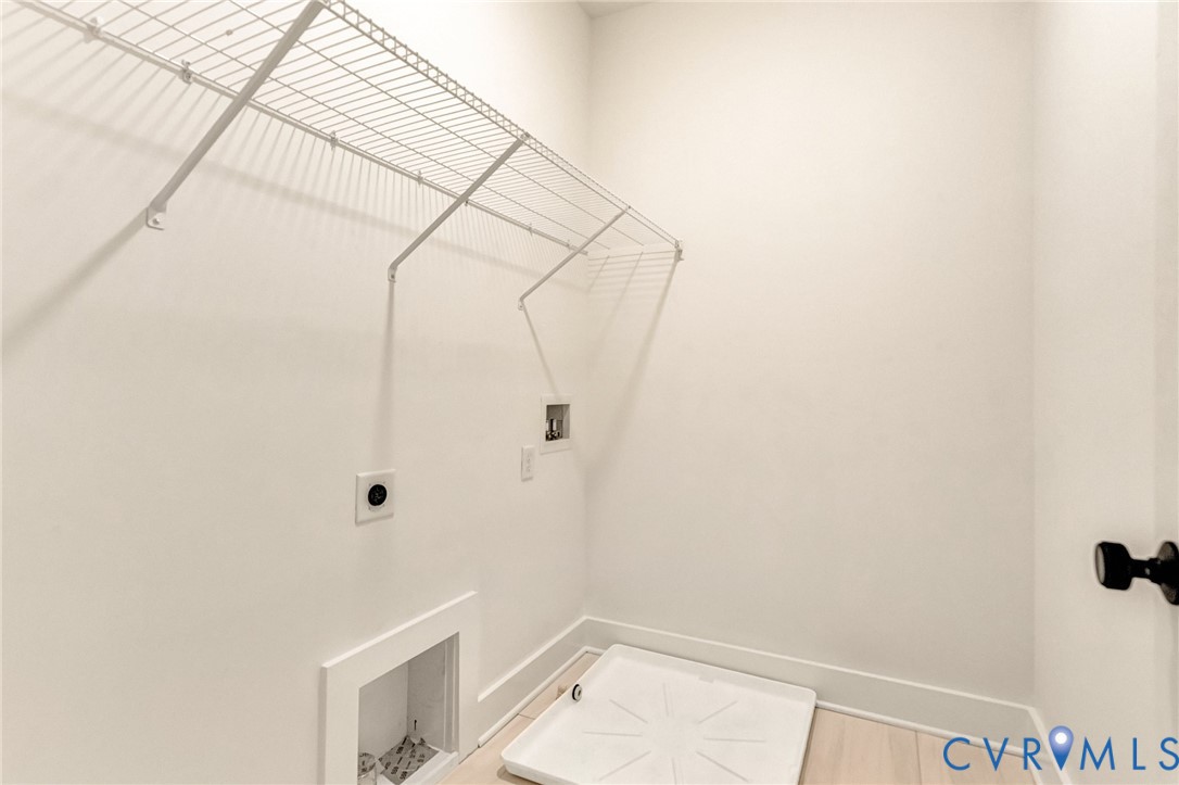 Utility space featuring a white drain pan, white wall-mounted shelving, and designated water and electrical hookups