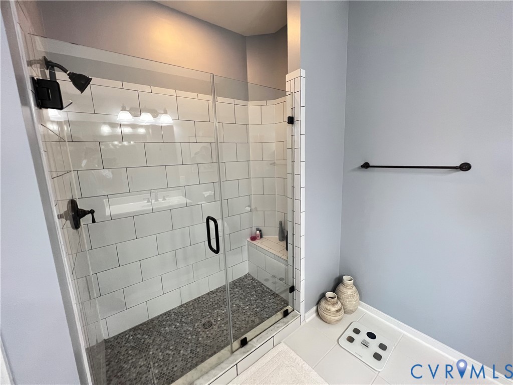 Walk-in shower featuring a glass enclosure, white subway tile surround, pebble-style floor tiling, built-in corner bench, and matte black fixtures
