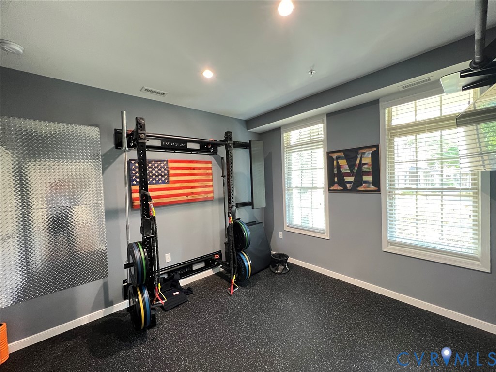 Room featuring dark speckled rubber flooring, recessed ceiling lighting, two double-hung windows with integrated blinds, and diamond-plate metal wall paneling Room featuring dark speckled rubber flooring, recessed ceiling lighting, two double-hung windows with integrated blinds, and diamond-plate metal wall paneling