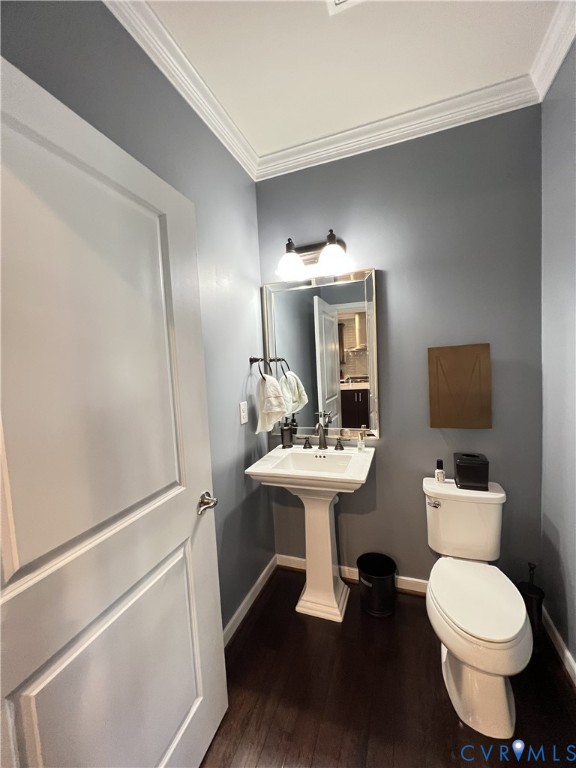 Pedestal sink with widespread metal faucet, framed rectangular mirror, crown molding, and wood-finish flooring