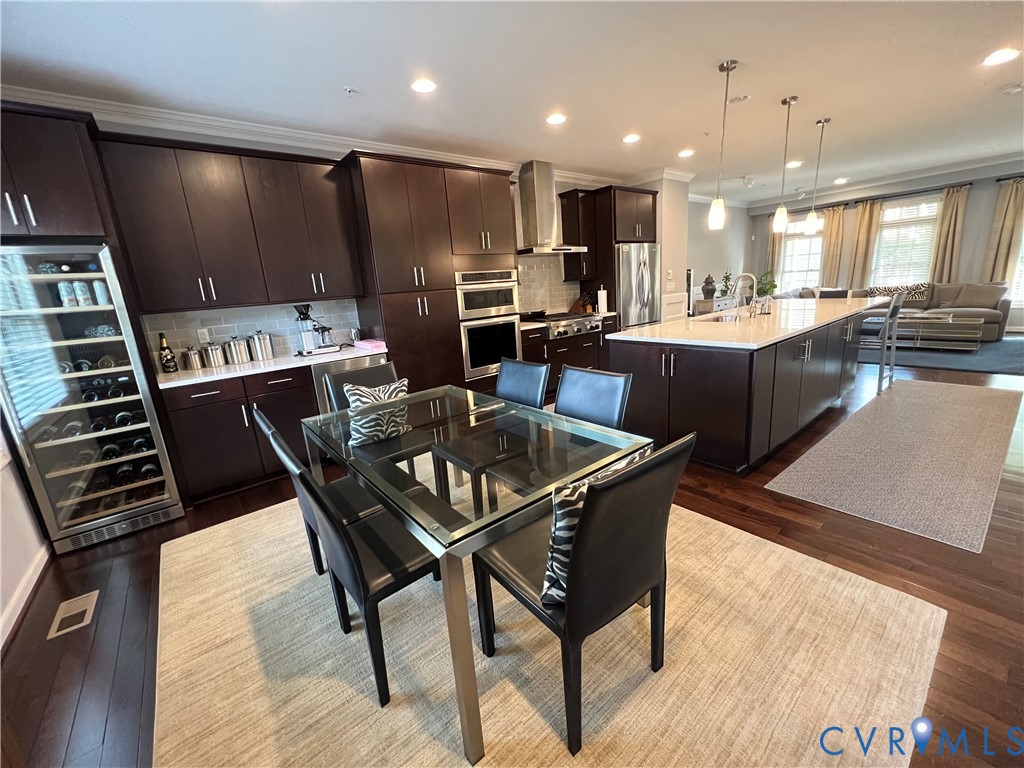 Kitchen featuring dark wood cabinetry, a large center island with a white countertop, built-in stainless steel appliances, a recessed wine cooler, and dark wood-finish flooring Kitchen featuring dark wood cabinetry, a large center island with a white countertop, built-in stainless steel appliances, a recessed wine cooler, and dark wood-finish flooring