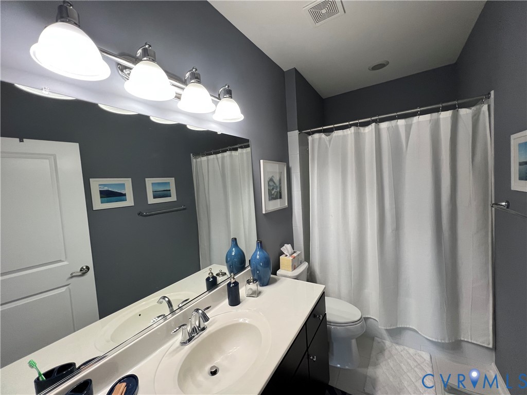 Vanity with a solid-surface countertop and integrated sink, four-light vanity fixture, expansive wall-mounted mirror, and a tub-shower combination with a shower rod