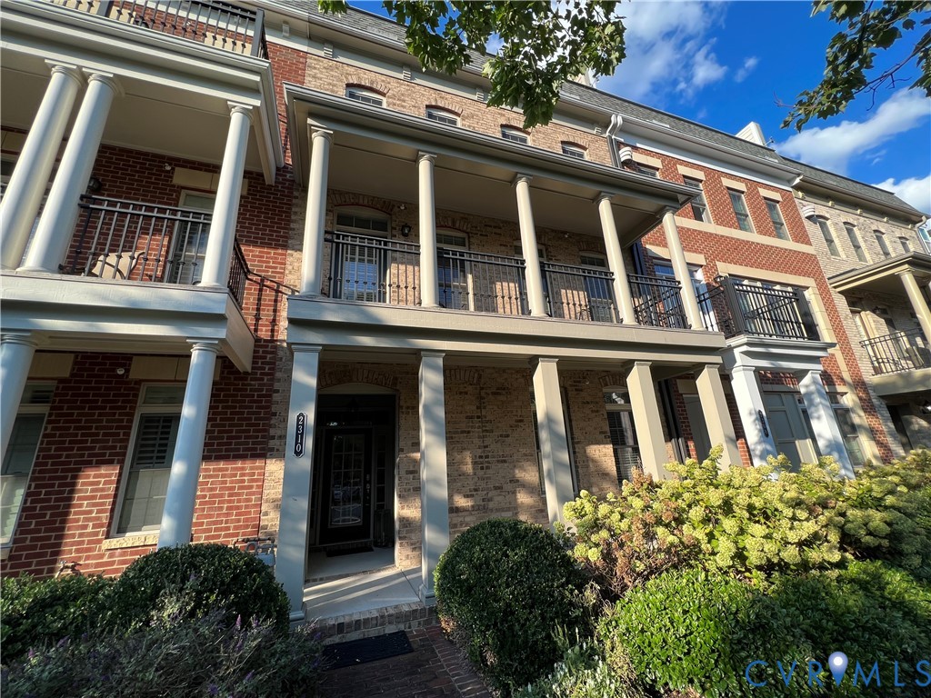 Multi-story brick exterior featuring a covered porch with classical columns, a second-story balcony with decorative metal railing, and a multi-pane glass entry door Multi-story brick exterior featuring a covered porch with classical columns, a second-story balcony with decorative metal railing, and a multi-pane glass entry door