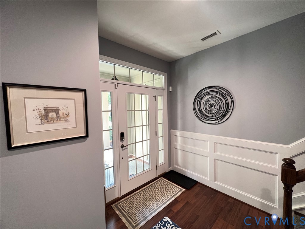 Entryway featuring white grid-paneled doors with an oversized transom window, extensive wainscoting, and wood-finish flooring Entryway featuring white grid-paneled doors with an oversized transom window, extensive wainscoting, and wood-finish flooring