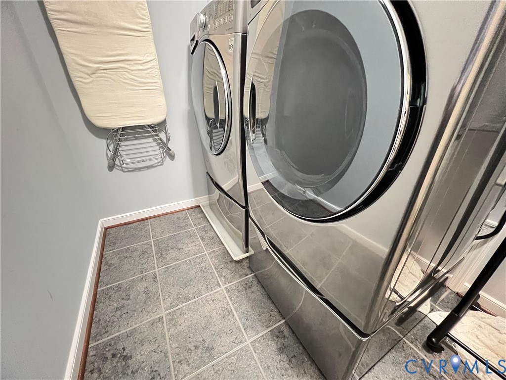Utility space featuring large-format ceramic tile flooring and stainless steel front-load laundry appliances