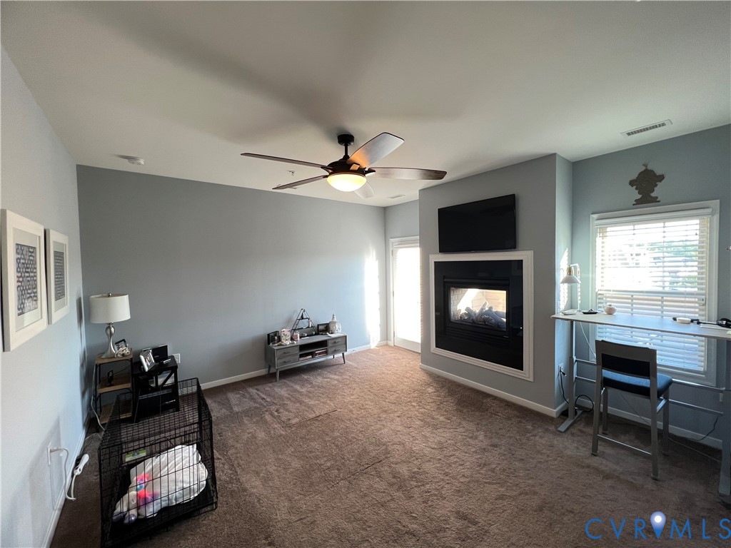 Built-in fireplace with a black surround, ceiling fan with integrated lighting, window with horizontal blinds, and carpeted flooring