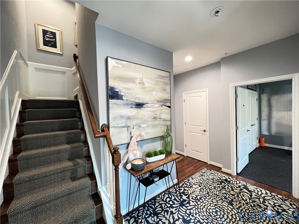 Foyer featuring wood-finish flooring, staircase with patterned carpeting, recessed lighting, and wall paneling Foyer featuring wood-finish flooring, staircase with patterned carpeting, recessed lighting, and wall paneling