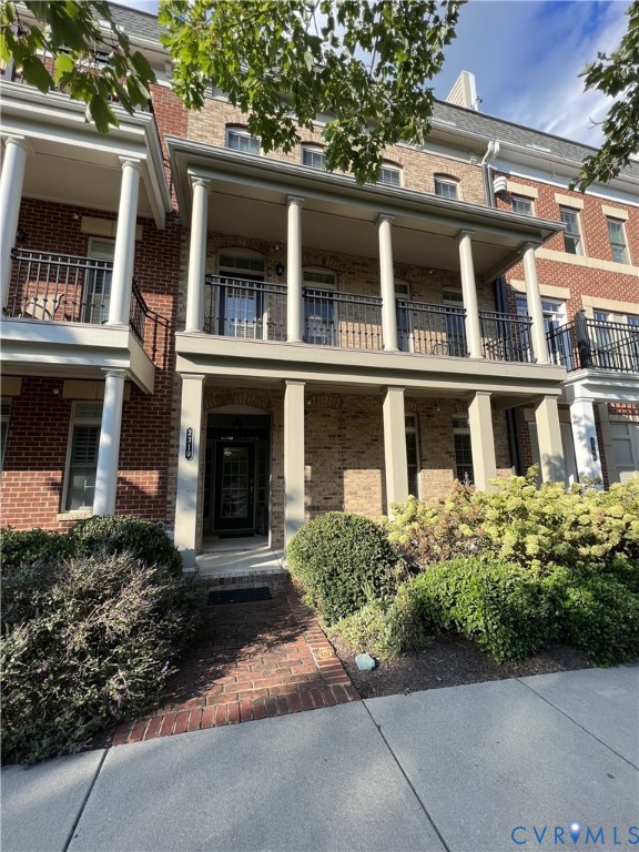 Multi-story brick exterior featuring a covered front porch with classic columns, second-level railed balcony, and decorative brick masonry detail