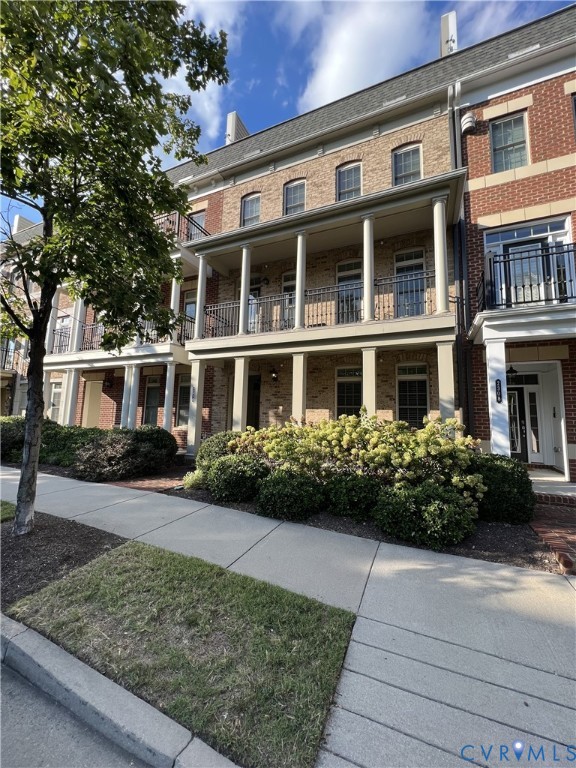 Multi-story brick exterior featuring a covered porch with structural columns and a metal-railed balcony Multi-story brick exterior featuring a covered porch with structural columns and a metal-railed balcony