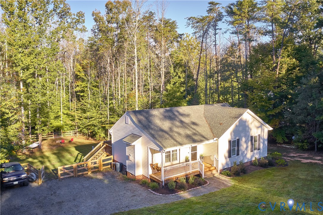 Single-story residence featuring light-colored horizontal siding, an asphalt shingle roof, a covered front porch with railing, a gravel driveway, and a fenced side yard area