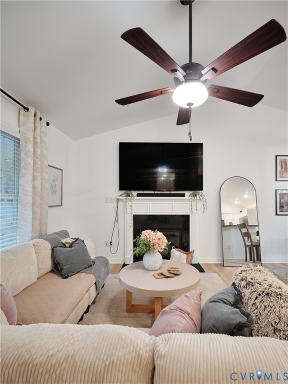 Vaulted ceilings, white fireplace mantle, dark-finish ceiling fan with integrated lighting, and neutral wall tones