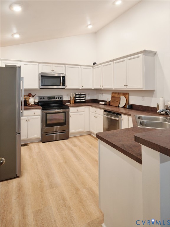 Kitchen featuring white cabinetry, solid-surface countertops, stainless steel appliances, and wood-finish flooring