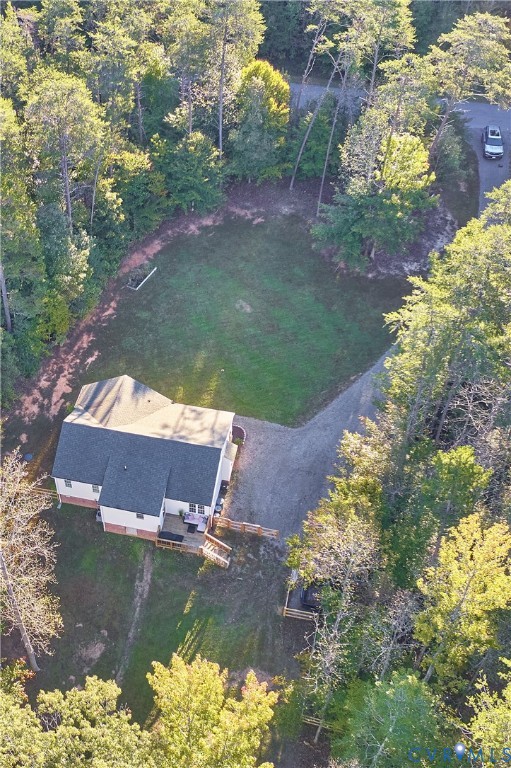 Aerial perspective of a detached residence featuring a gravel driveway, wood-framed rear deck, and expansive grounds surrounded by mature trees