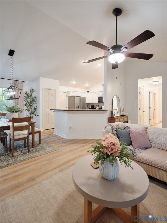 Open-concept interior featuring vaulted ceilings, wood-finish flooring, a matte black multi-light pendant fixture, and a ceiling fan with dark wood-finish blades