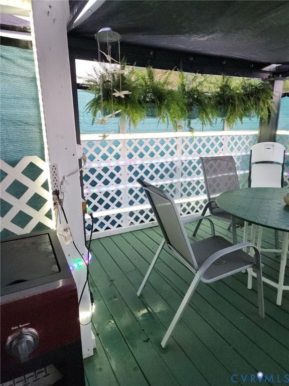Covered outdoor deck featuring painted wood-finish decking, white latticework railing, and an overhead structural frame