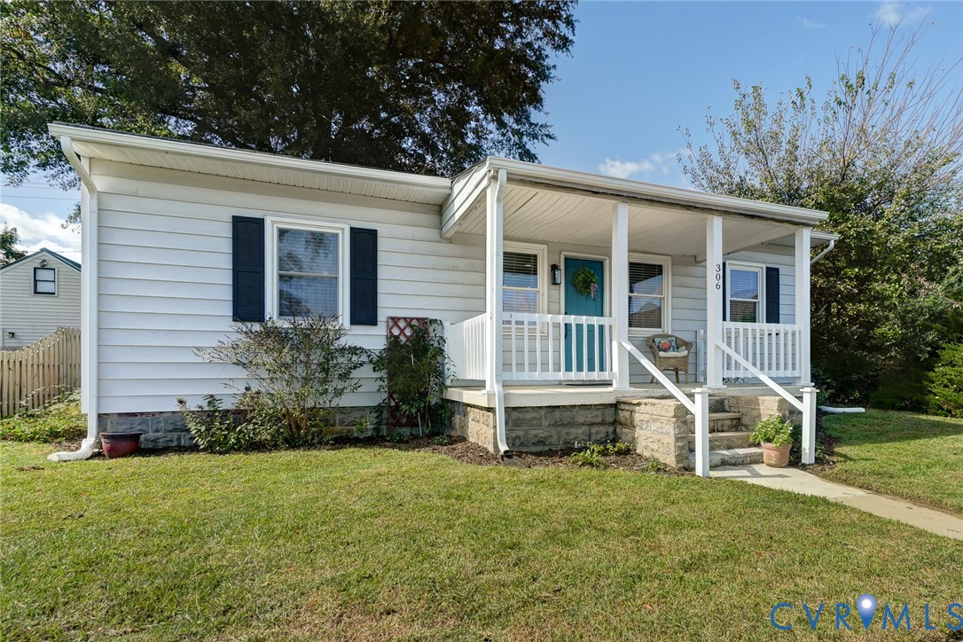 Single-story exterior featuring light-colored horizontal siding, a covered front porch with white railing, stone foundation detailing, and contrasting dark window shutters