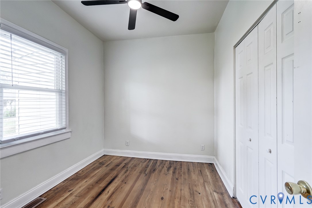 Room interior featuring wood-finish flooring, a multi-panel door closet, a window with horizontal blinds, and a ceiling-mounted fan