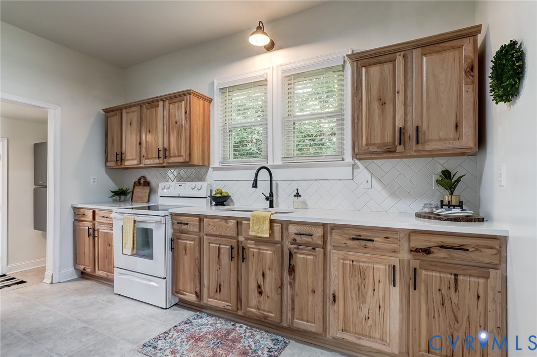 Kitchen featuring custom wood cabinetry, white countertops, herringbone-patterned tile backsplash, matte black hardware, and a single-handle pull-down faucet