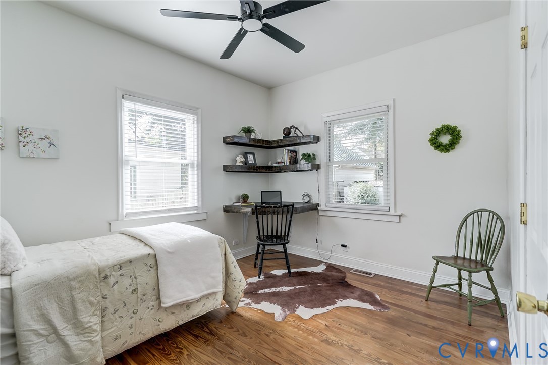 Wood-finish flooring, matte black ceiling fan, dual windows with horizontal blinds, and built-in corner shelving