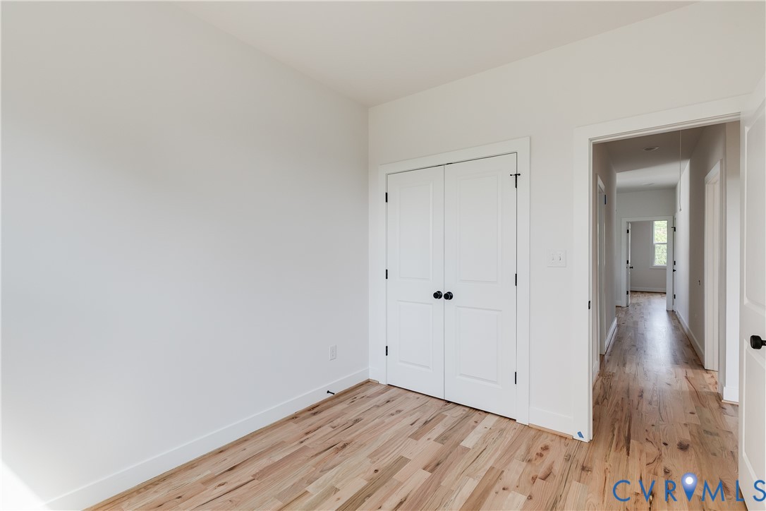 Neutral-toned walls, wood-finish flooring, and white double-panel closet doors featuring matte black hardware