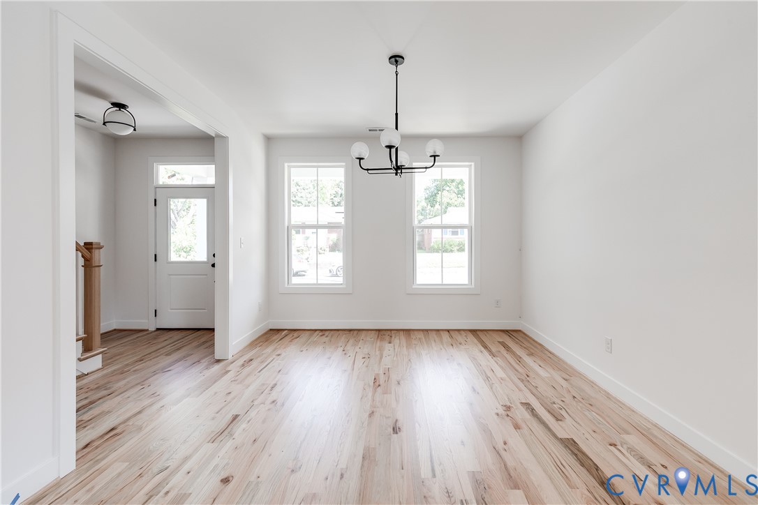Bright interior featuring wood-finish flooring, two double-hung windows, a tiered multi-globe chandelier, and an exterior door with a transom window Bright interior featuring wood-finish flooring, two double-hung windows, a tiered multi-globe chandelier, and an exterior door with a transom window