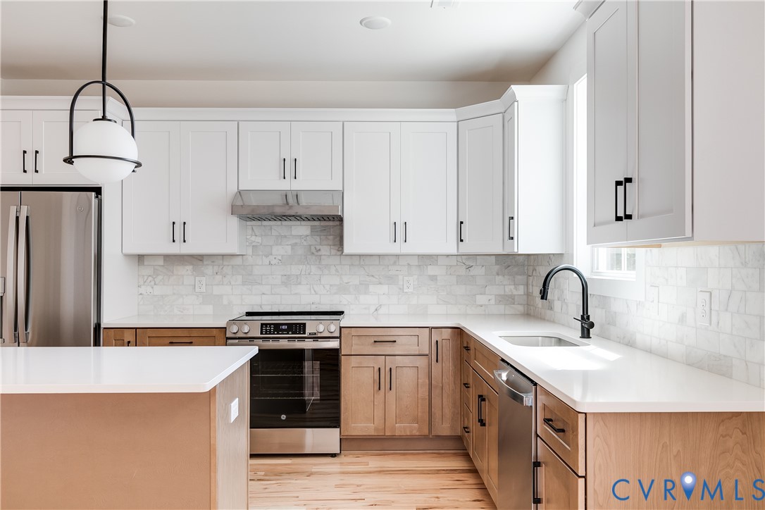 Kitchen featuring two-tone cabinetry, stone tile backsplash, stainless steel appliances, white solid-surface countertops, and a spherical pendant light fixture