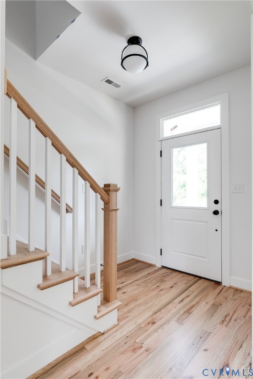 Foyer featuring wood-finish flooring, a white paneled door with a transom window, and a staircase with a natural wood handrail and square balusters Foyer featuring wood-finish flooring, a white paneled door with a transom window, and a staircase with a natural wood handrail and square balusters