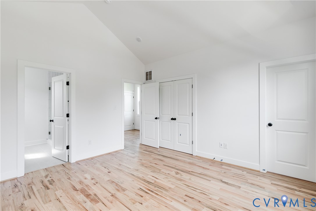 Vaulted ceiling, wood-finish flooring, double-panel closet doors, and solid-core interior doors with matte black hardware