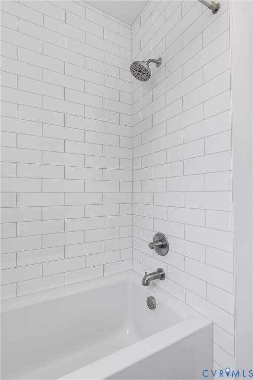 Bathtub enclosure featuring white subway tile wall surround, brushed nickel shower head, matching tub spout, and integrated mixing valve