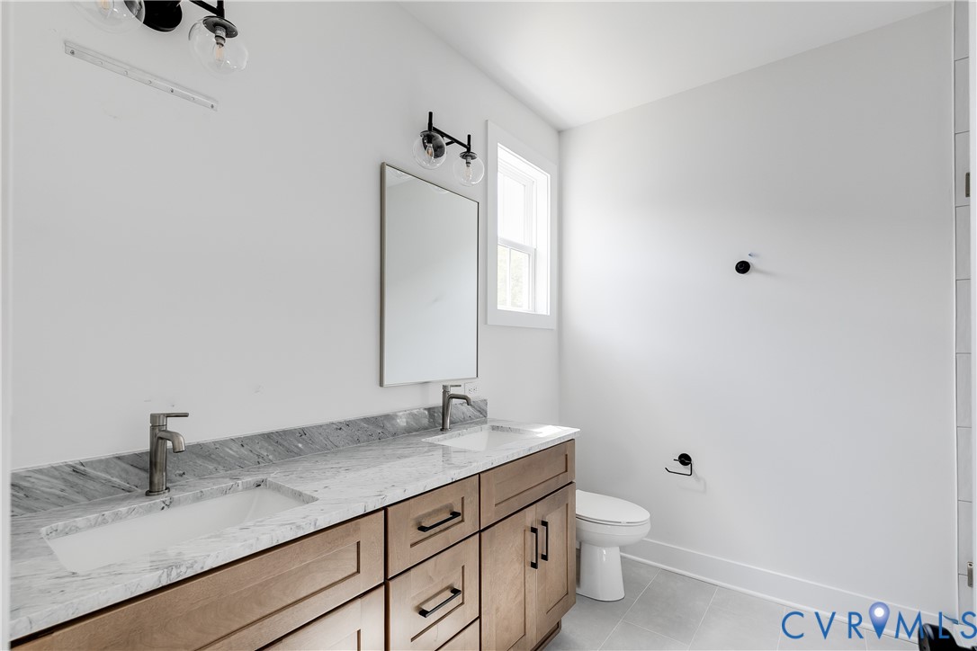 Dual-sink vanity featuring stone countertops, under-mount sinks, wood-finish cabinetry, and matte black fixtures