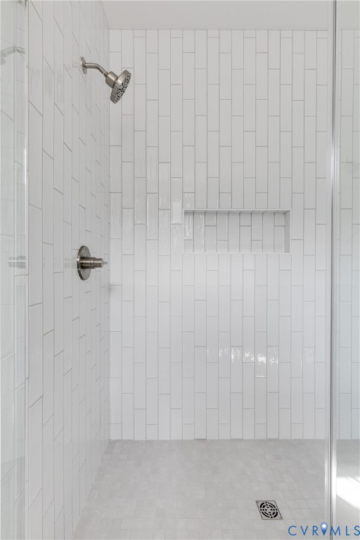 Walk-in shower featuring vertical white subway tile, brushed nickel showerhead and control valve, built-in recessed storage niche, and light-toned tile flooring