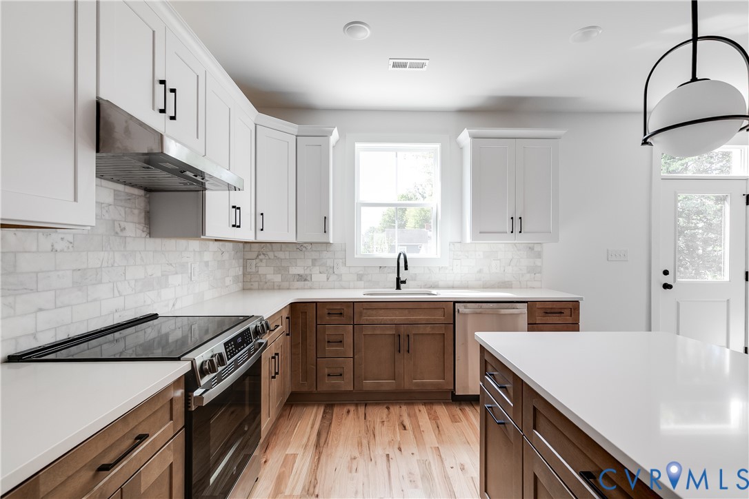 Kitchen featuring two-tone cabinetry, stone tile backsplash, white quartz countertops, stainless steel appliances, and wood-finish flooring