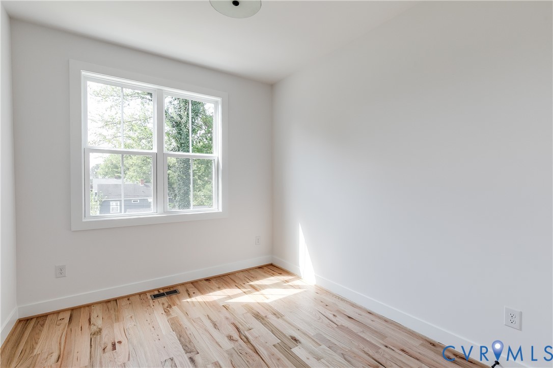 Room featuring wood-finish flooring, white walls, and a double-hung window with muntins
