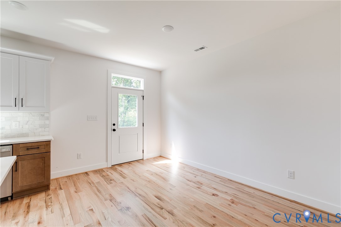 Kitchen area featuring light-toned wood-finish flooring, two-tone cabinetry with contrasting upper and lower finishes, stone-tiled backsplash, and a six-panel exterior door with a transom window