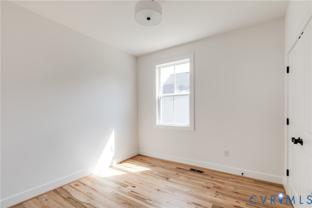 Room featuring wood-finish flooring, a single-hung window, a drum-style ceiling light fixture, and a paneled door with matte black hardware