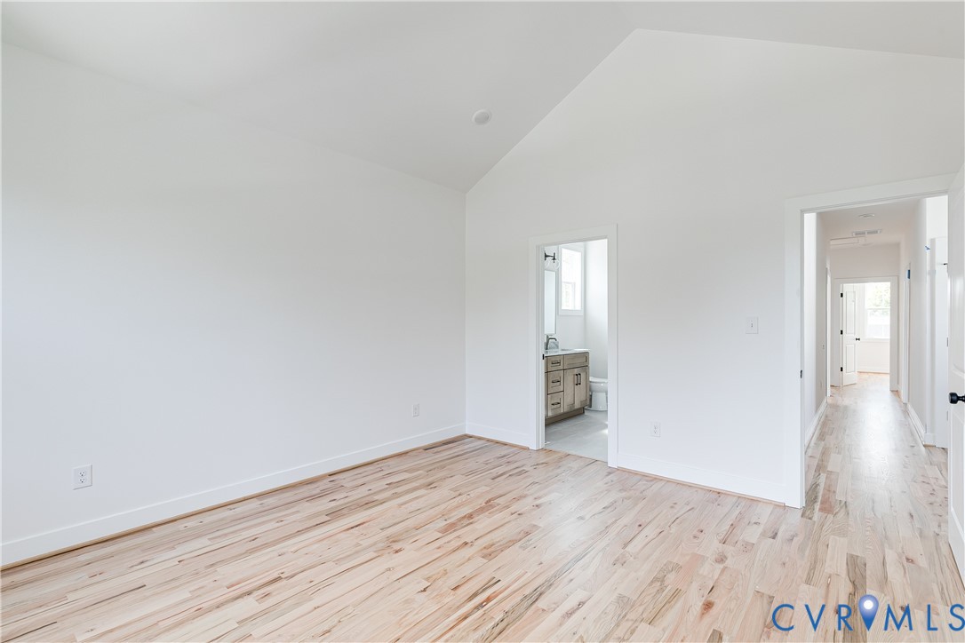 Room featuring vaulted ceilings, light-toned wood-finish flooring, and crisp white wall paint