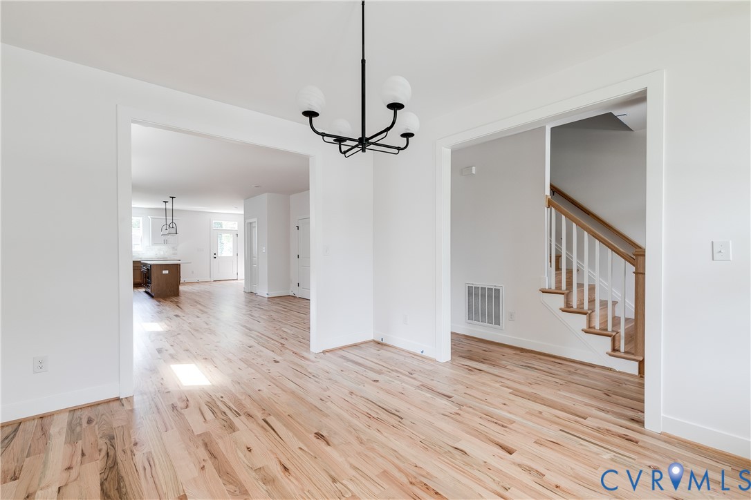 Wood-finish flooring throughout, matte black multi-light chandelier, and staircase featuring white balusters with a natural wood-tone handrail Wood-finish flooring throughout, matte black multi-light chandelier, and staircase featuring white balusters with a natural wood-tone handrail