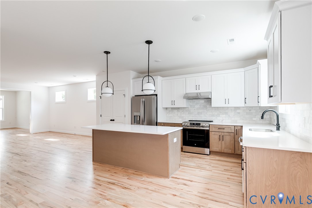 Kitchen featuring white upper cabinetry, lower wood-finish cabinetry, an oversized center island with quartz countertops, two modern globe pendant lights, and stainless steel appliances Kitchen featuring white upper cabinetry, lower wood-finish cabinetry, an oversized center island with quartz countertops, two modern globe pendant lights, and stainless steel appliances