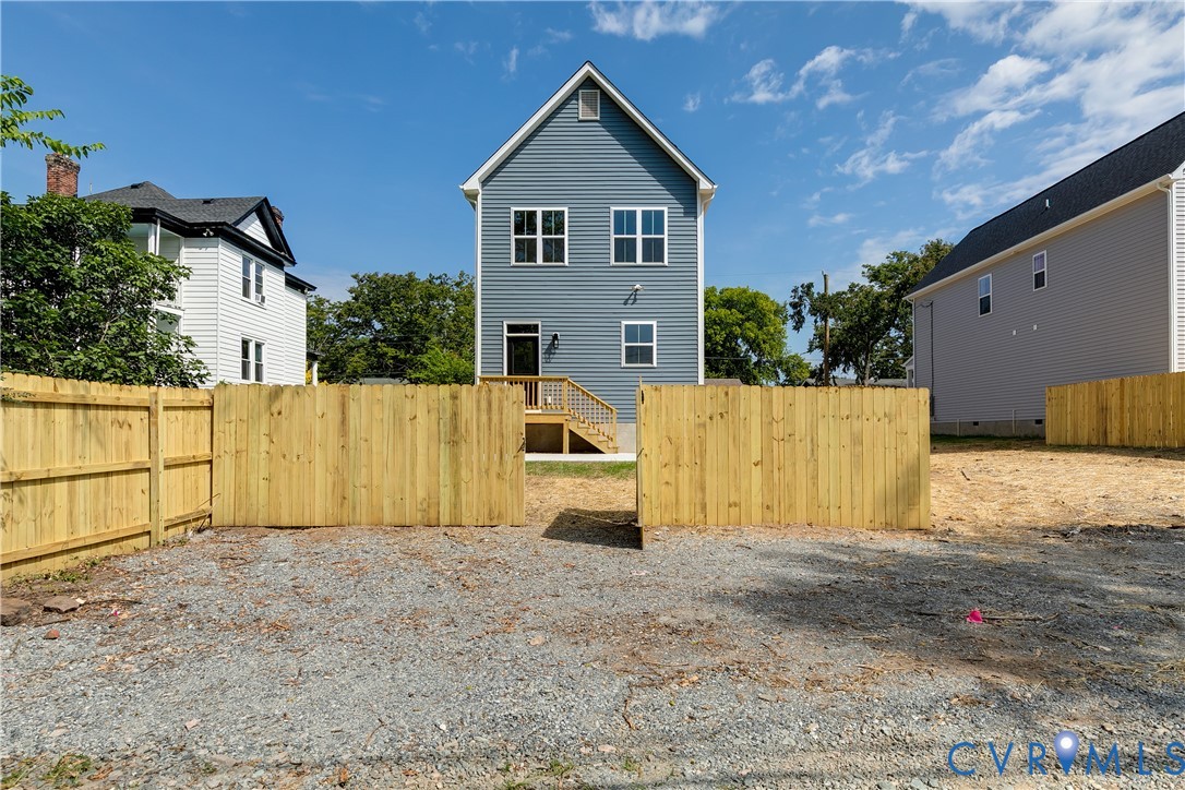 Two-story residence with horizontal siding, a gable roofline, elevated rear wood deck, and a fenced backyard area featuring gravel surfacing