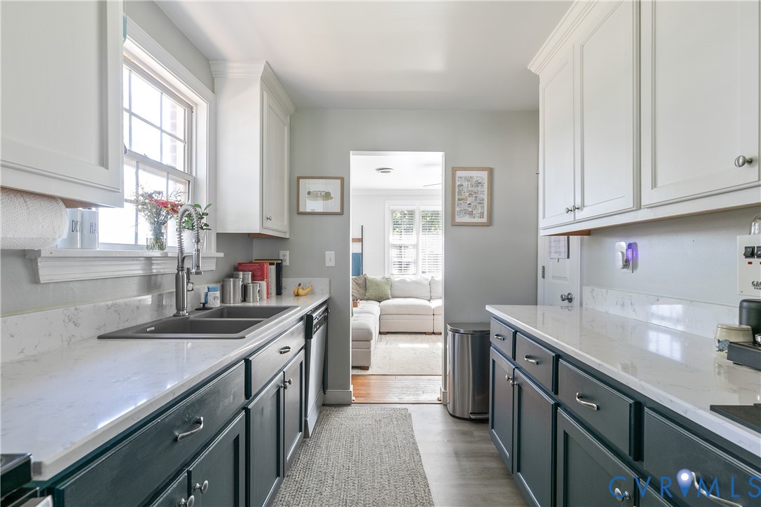 Kitchen featuring dual-toned cabinetry, quartz countertops, a double-basin stainless steel sink with a high-arch faucet, and wood-finish flooring